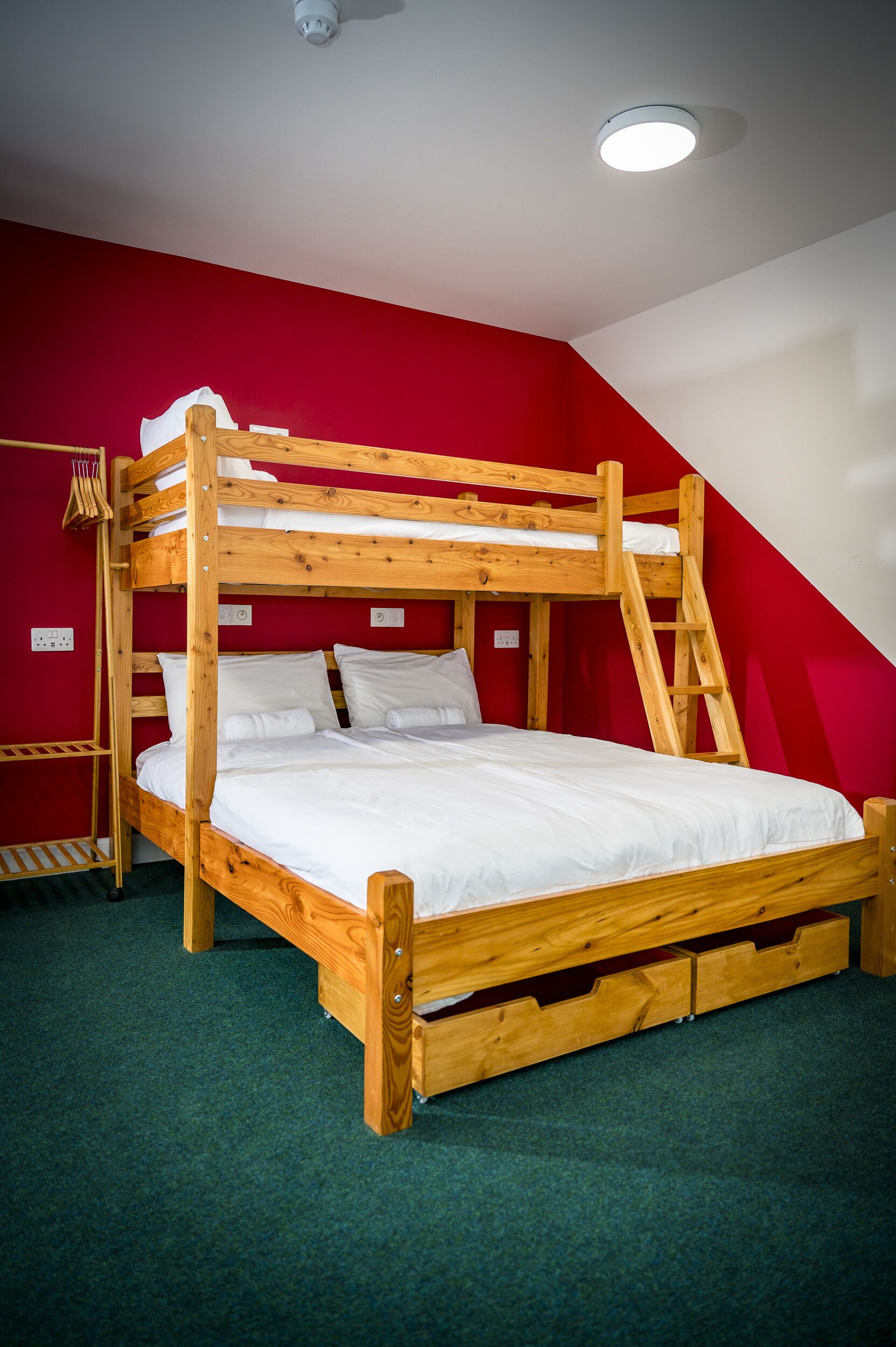 A bunk bed with a ladder, white bedding, and a red wall.