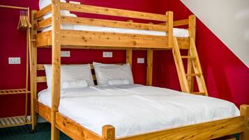 A bunk bed with a ladder, white bedding, and a red wall.