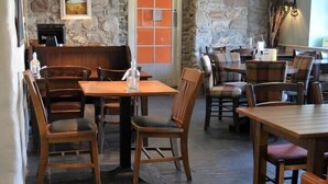 A restaurant with wooden tables and chairs, stone walls, and a stone fireplace.