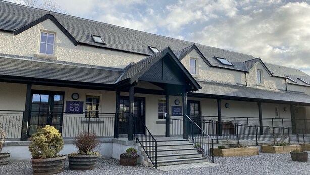 A building with a grey roof, multiple windows, and a sign indicating room availability.