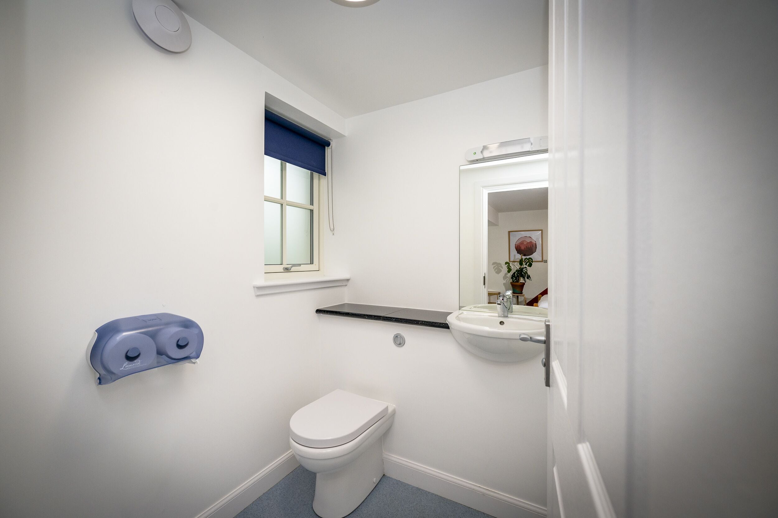 A bathroom with a toilet, a sink, a mirror, and a window with a blue blind.