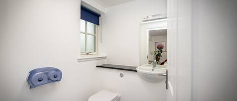 A bathroom with a toilet, a sink, a mirror, and a window with a blue blind.