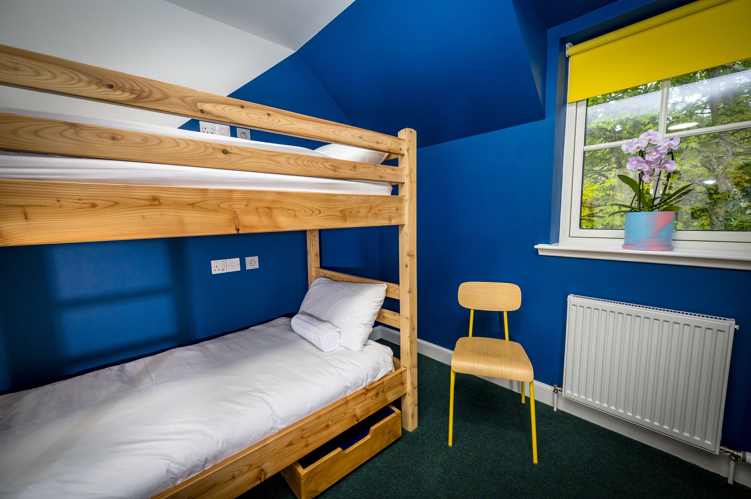 Un lit superposé avec une structure en bois, un matelas blanc et une chaise en bois.