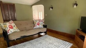 A room with a sofa, a patterned rug, wooden flooring, a television, and wall-mounted lights.