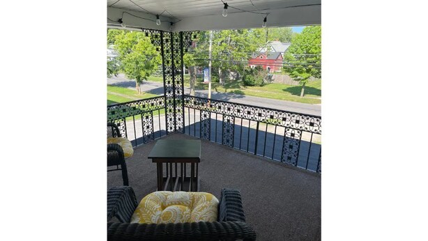 A covered balcony with outdoor furniture, a metal railing, and a view of a residential street.