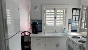 A compact kitchen with white cabinets, a stove, a sink, and a window.