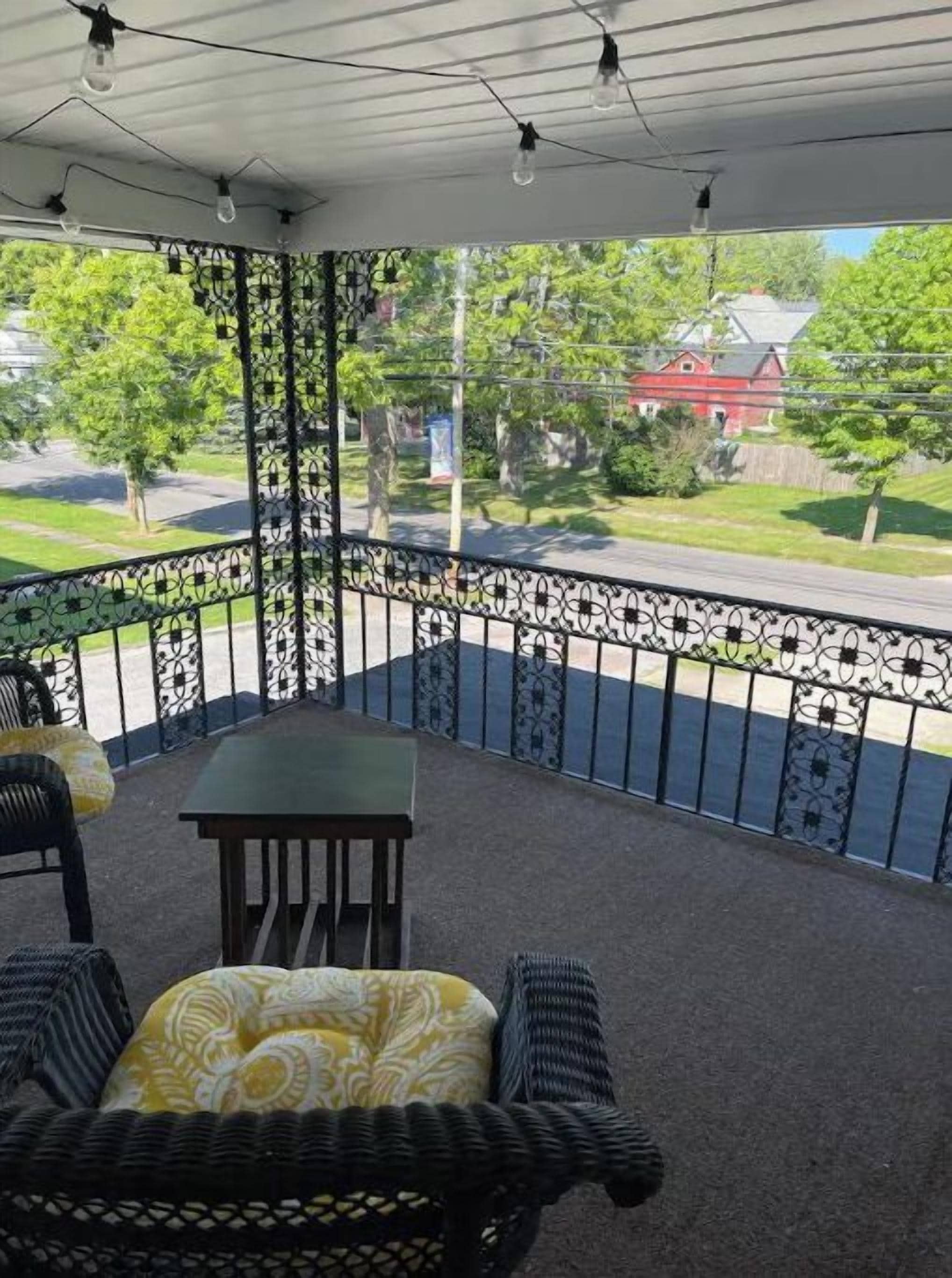 Ein überdachter Balkon mit Gartenmöbeln, einem Metallgeländer und Blick auf eine Wohnstraße.
