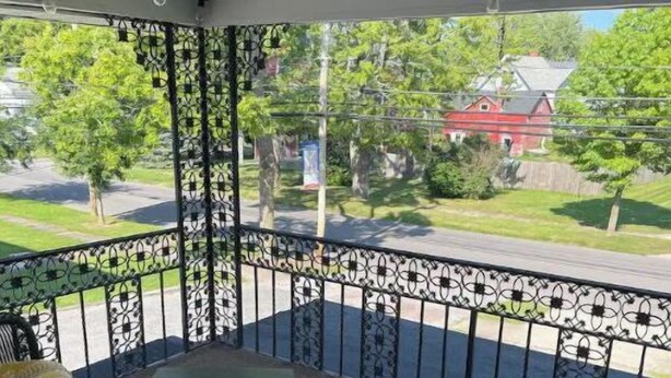 Ein überdachter Balkon mit Gartenmöbeln, einem Metallgeländer und Blick auf eine Wohnstraße.