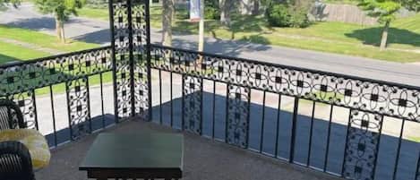 Ein überdachter Balkon mit Gartenmöbeln, einem Metallgeländer und Blick auf eine Wohnstraße.