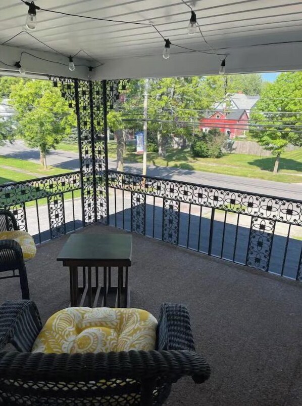 Un balcon abrité, doté de mobilier d’extérieur, d’une rambarde en métal et offrant une vue sur une rue résidentielle.