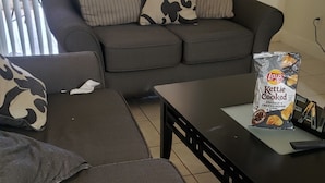 Un salon comprenant un canapé, deux fauteuils, une table basse et un paquet de chips Lay's, saveur sel de mer et poivre concassé.
