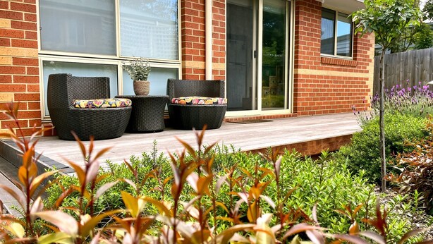 Una casa de ladrillo con un porche cubierto, muebles de mimbre y una planta en maceta.