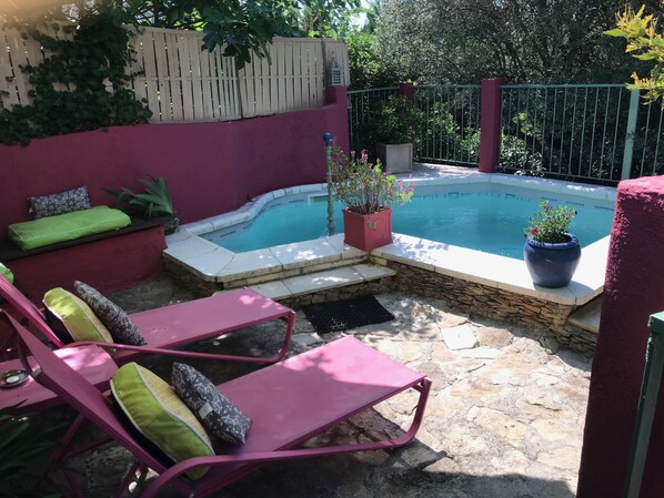 A backyard with a swimming pool, stone flooring, and pink lounge chairs.