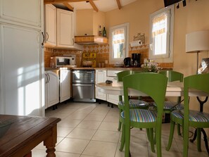A kitchen with white cabinets, a microwave, a coffee maker, and a sign that says "NOT A THROUGH." There are green chairs and a wooden table.