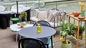 A rooftop terrace with a round table, chairs, a sofa, and potted plants. - Tribe Paris La Defense Esplanade (Courbevoie)