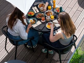 Dos personas sentadas en una mesa al aire libre, con distintos alimentos y bebidas para el desayuno.
