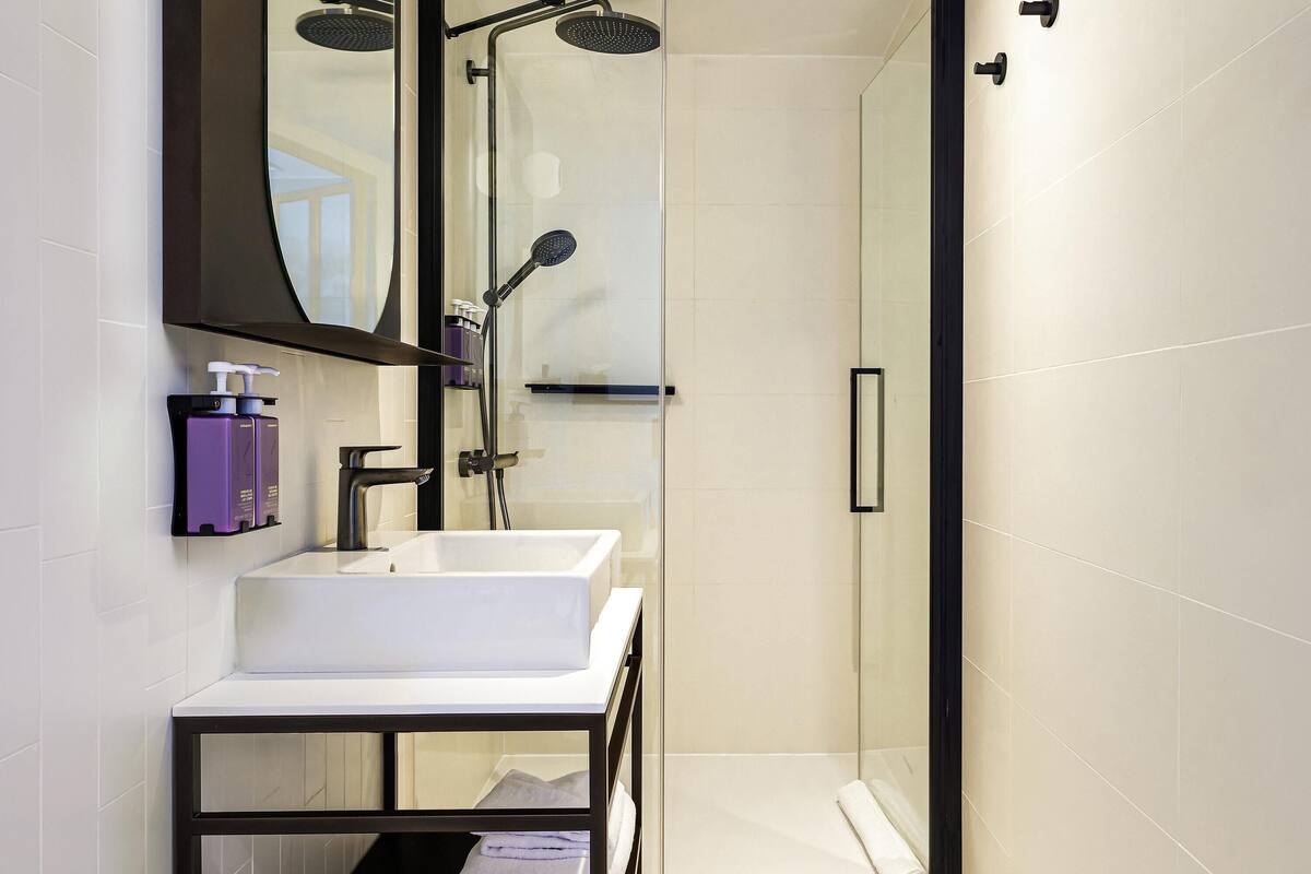 A modern bathroom with a white sink, black fixtures, and a glass shower enclosure.