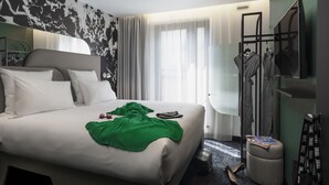A hotel room with a bed, a green throw blanket, a mirror, and a shoe rack. - Tribe Paris La Defense Esplanade (Courbevoie)
