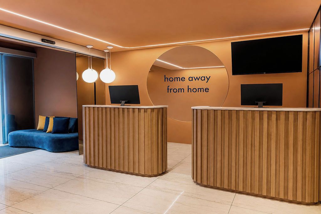 A reception area with two wooden reception desks, a blue sofa, and a large TV screen on the wall.