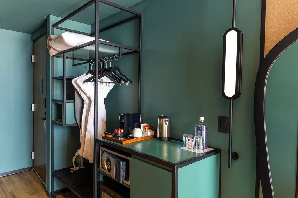 Une chambre compacte avec un lit superposé, un bureau équipé d’une bouilloire, d’une bouteille d’eau et d’un porte-manteau mural.