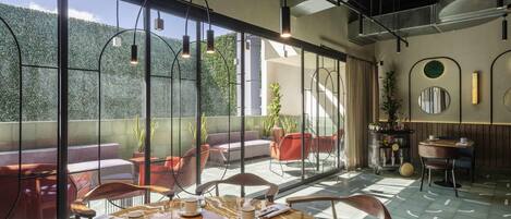 A modern dining area with a marble table, chairs, and a view of greenery through large windows.