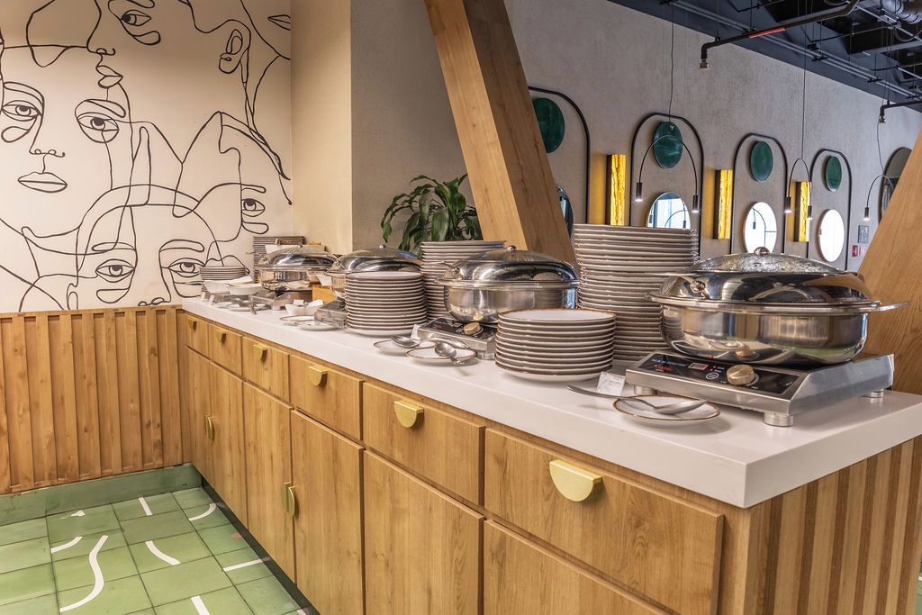 A kitchen area with stacked plates and pots, wooden cabinets, and a wall with abstract line drawings.