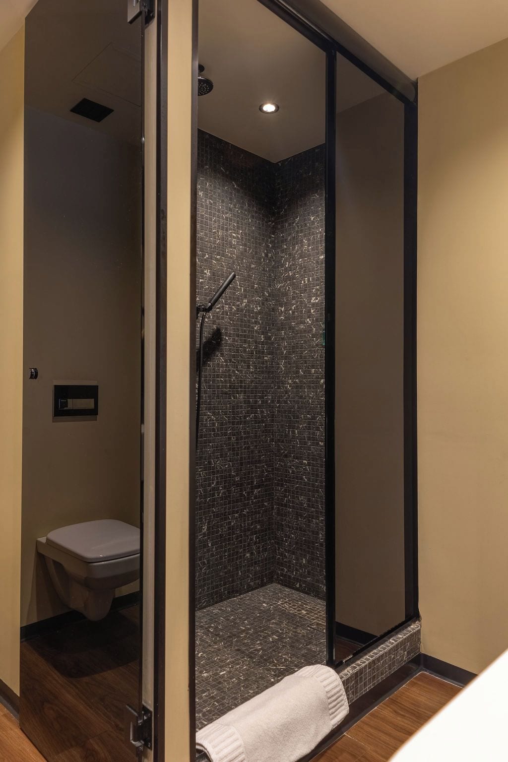 A modern bathroom with a shower, toilet, and a towel on the floor.