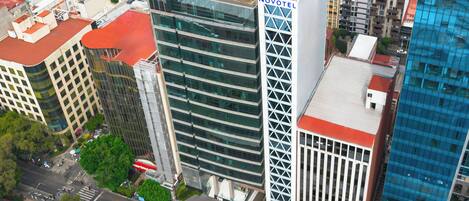 A high-rise building with a prominent 'NOVOTEL' sign, surrounded by other buildings and a street with vehicles and pedestrians.