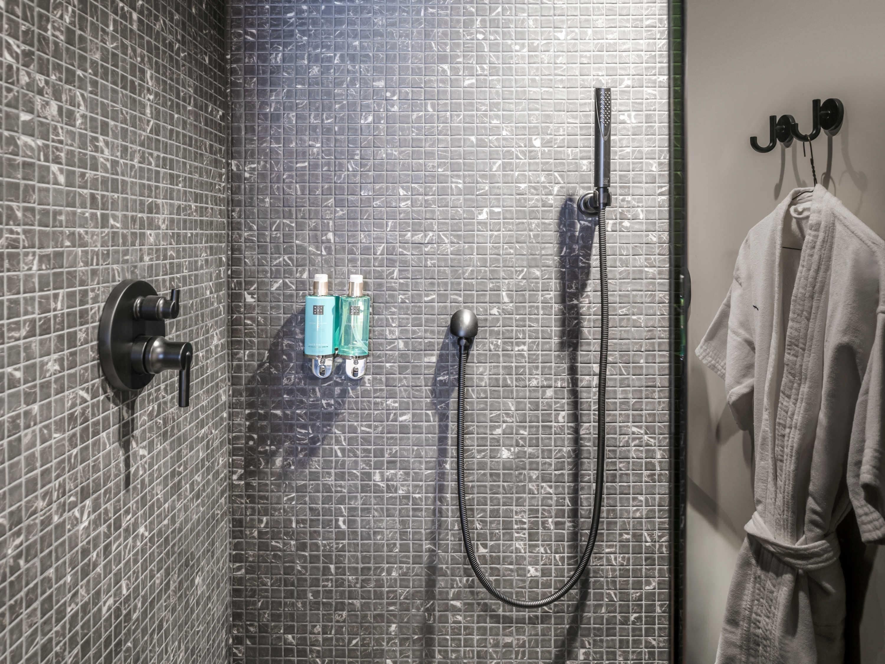 Une salle de bain avec un mur carrelé, une pomme de douche, deux bouteilles de shampoing et un porte-serviettes avec une serviette.