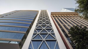 Un edificio moderno de gran altura con una fachada geométrica distintiva, amplios ventanales y una torre central imponente.