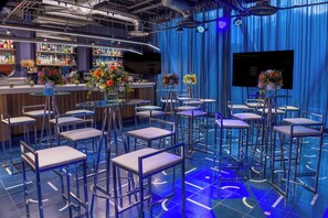 Un espace bar doté de plusieurs tabourets, d’un comptoir où sont exposées diverses bouteilles, et d’un écran de télévision fixé au mur.