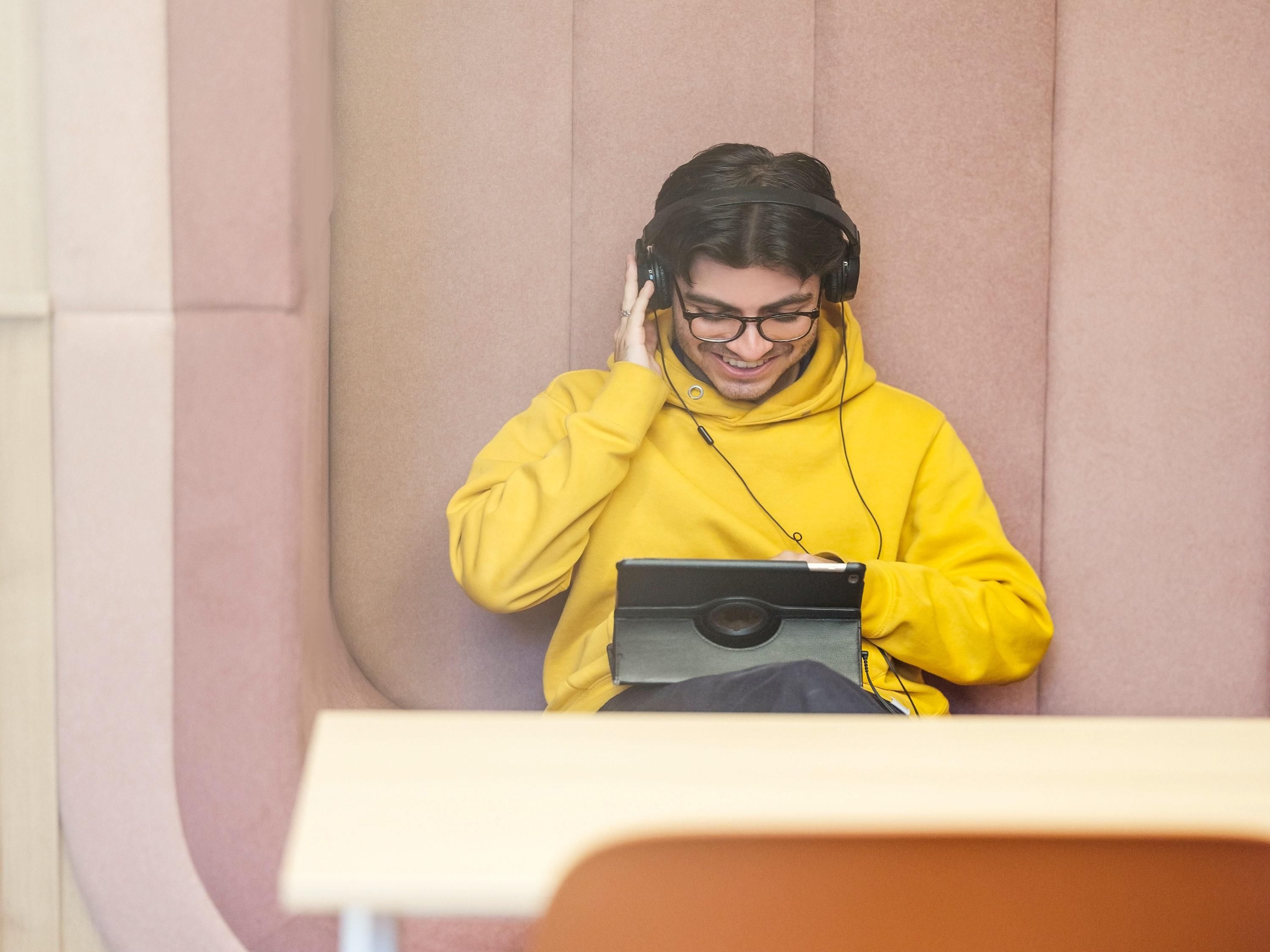 A person in a yellow hoodie using a laptop in a room with a beige wall and a white door.