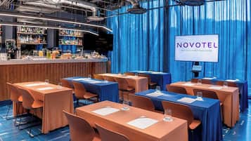 A hotel conference room with tables, chairs, a bar area, and a screen displaying the hotel name.