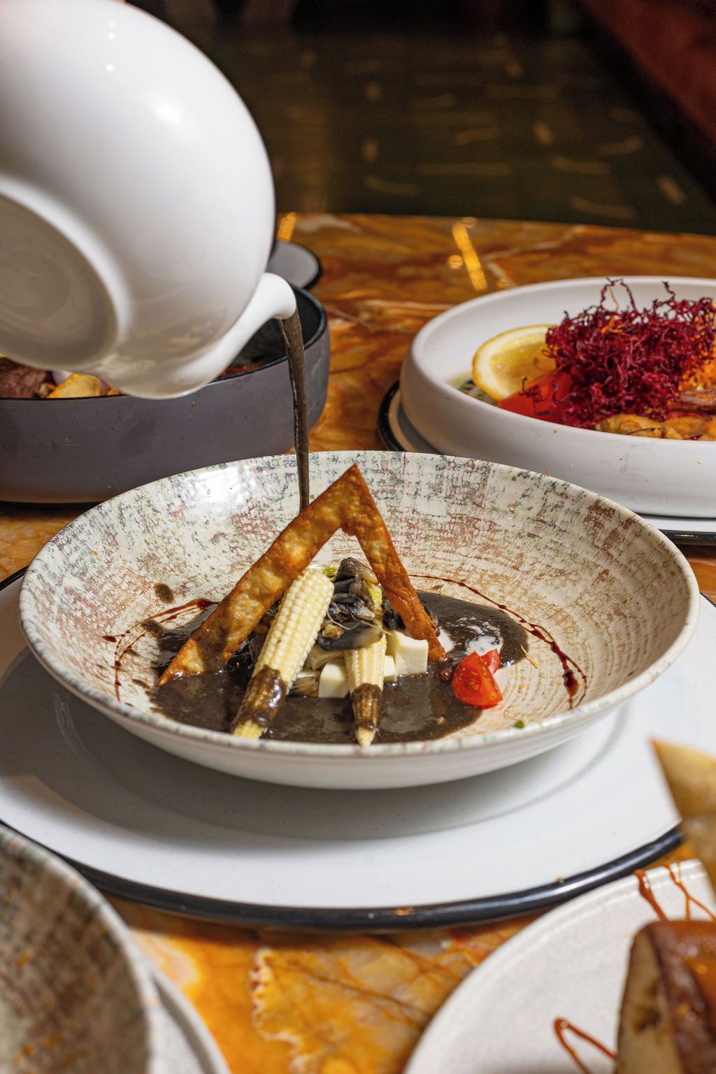 A dining table with a bowl of food, a white pitcher, and a plate with a lemon slice and red garnish.