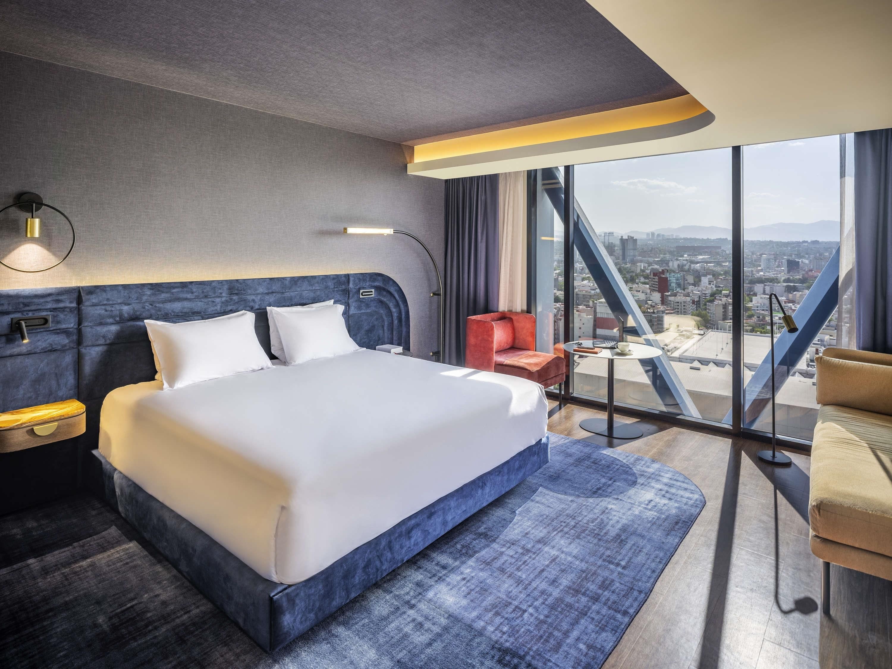 Une chambre d’hôtel moderne avec un grand lit, un bureau, une chaise et une vue sur la ville.