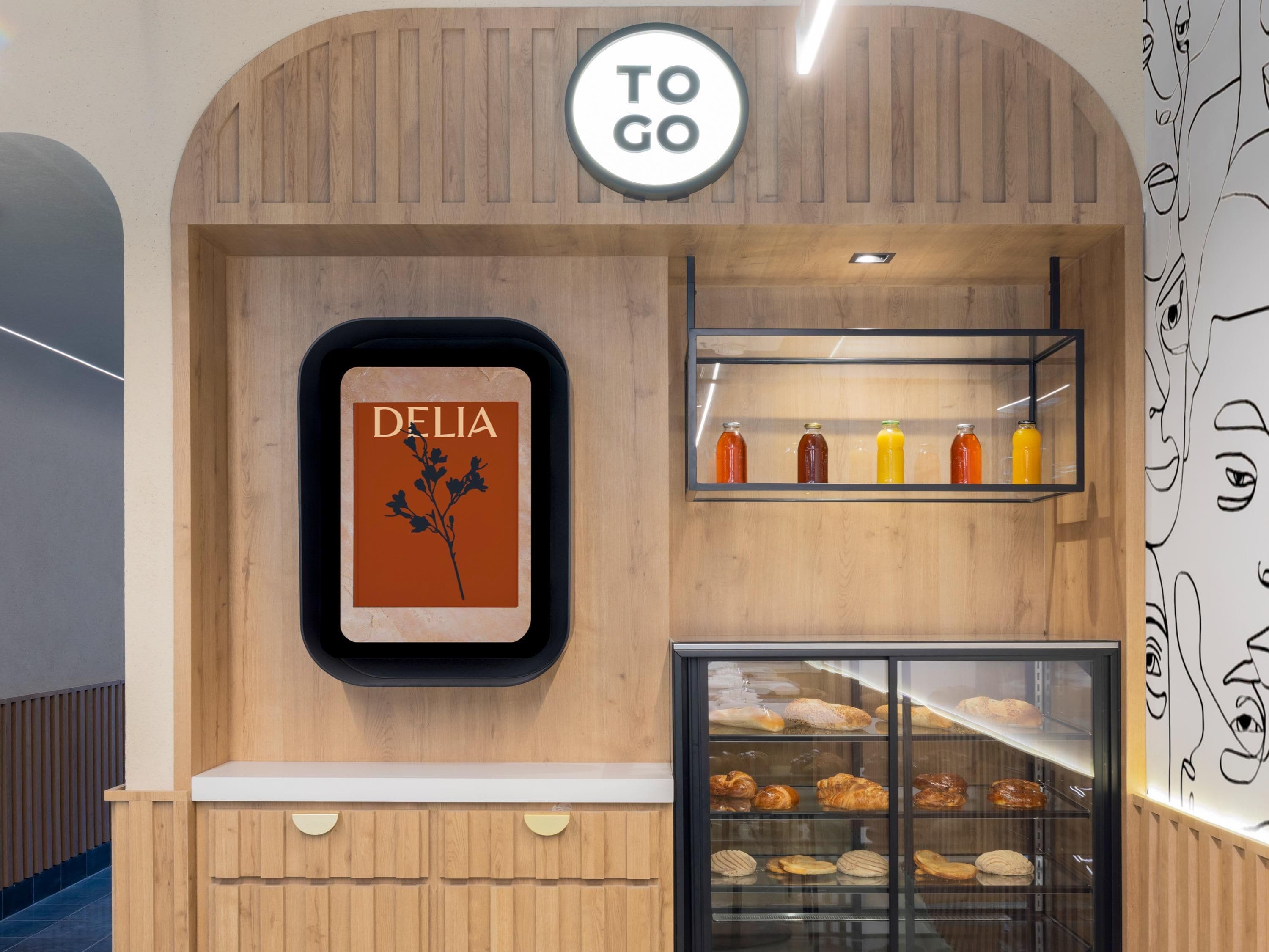 Een bakkerijdisplay met DELIA aanduiding, TO GO logo en diverse gebakken producten.