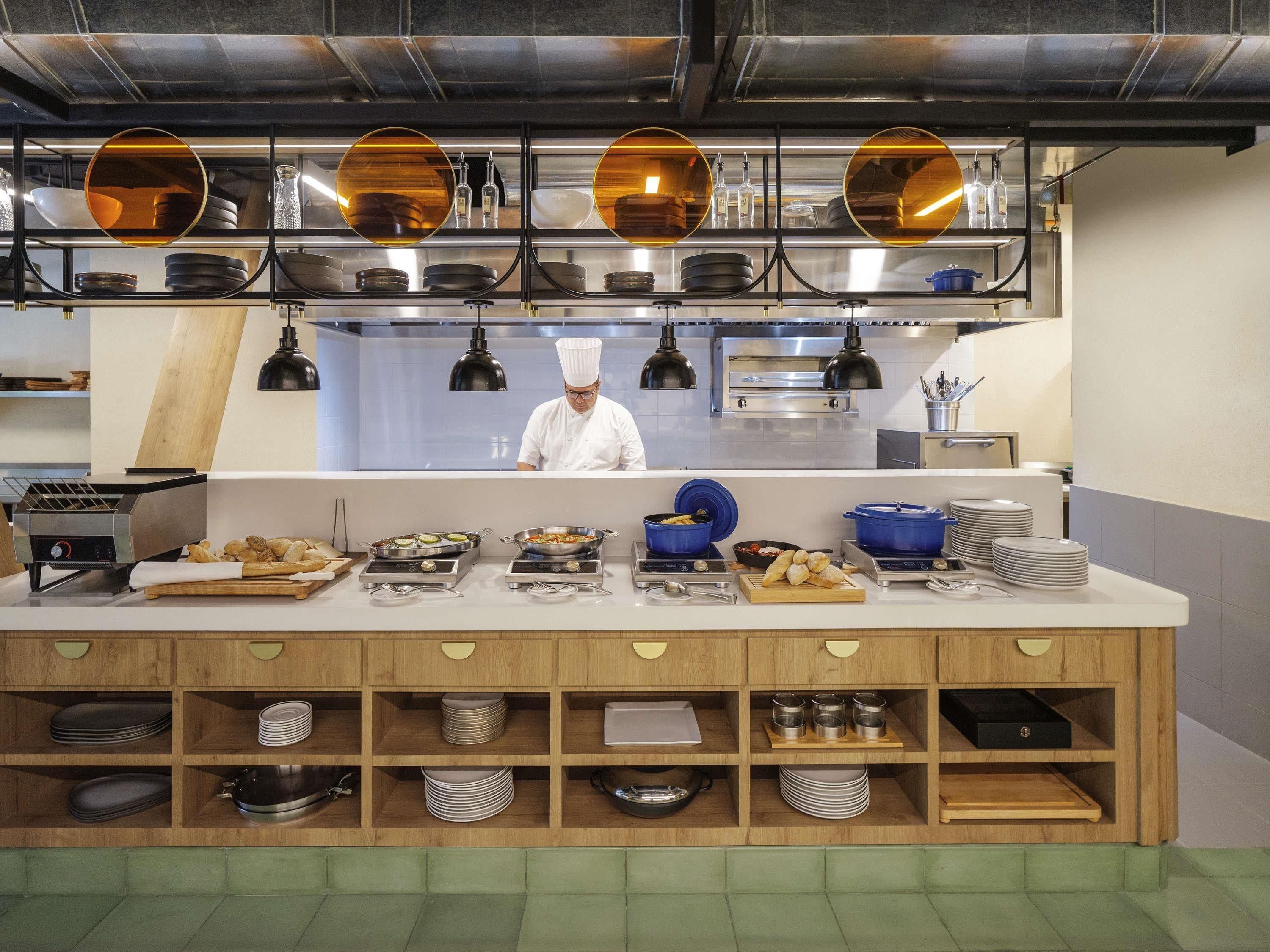 A modern kitchen with a chef at work, equipped with various cooking appliances and neatly organized utensils.