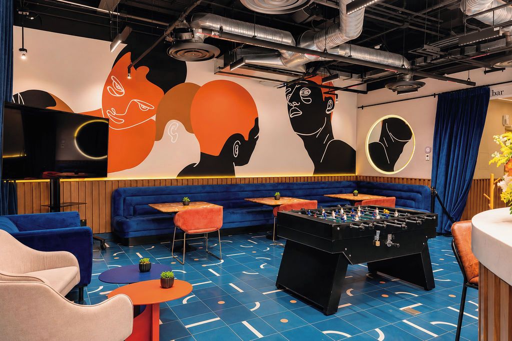 A room with a foosball table, sofas, and a wall mural.