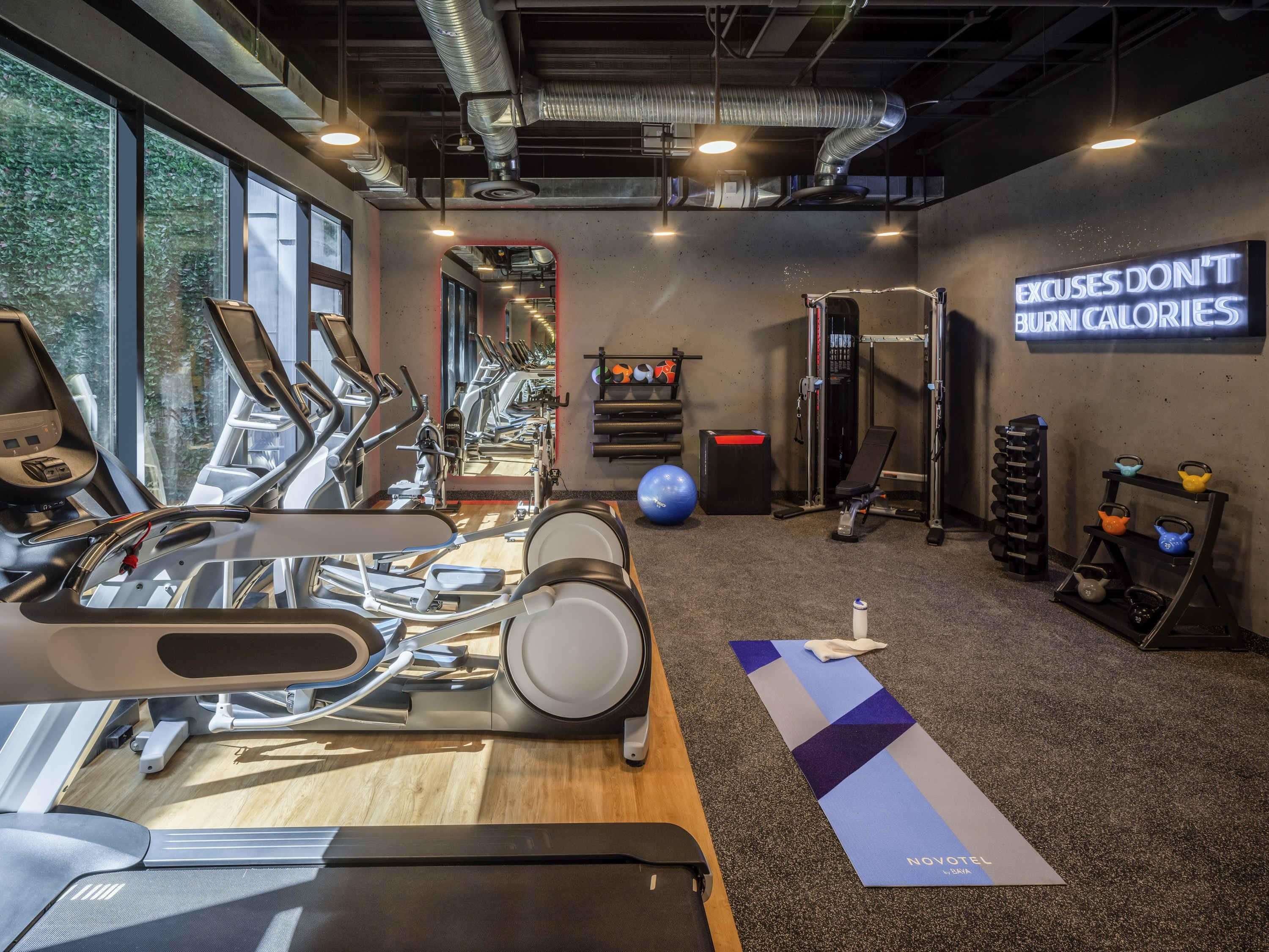 Une salle de sport équipée de tapis de course, d’un grand miroir fixé au mur, d’un porte-haltères et d’une affiche motivante.
