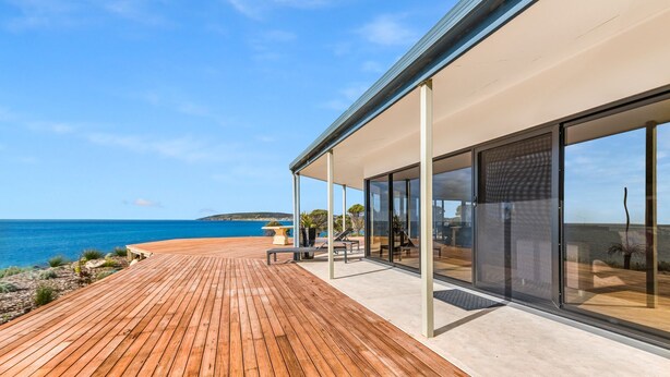 Et moderne hus med træterrasse med udsigt over havet, store glasvinduer og frit kig til kystlinjen.