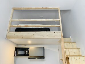A compact kitchen with a built-in microwave and oven, a wooden loft bed, and a small staircase.