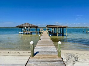 A wooden pier leading to two wooden structures with benches, overlooking clear blue water. - Comfy condo with Lagoon and Gulf access (Gulf Shores)