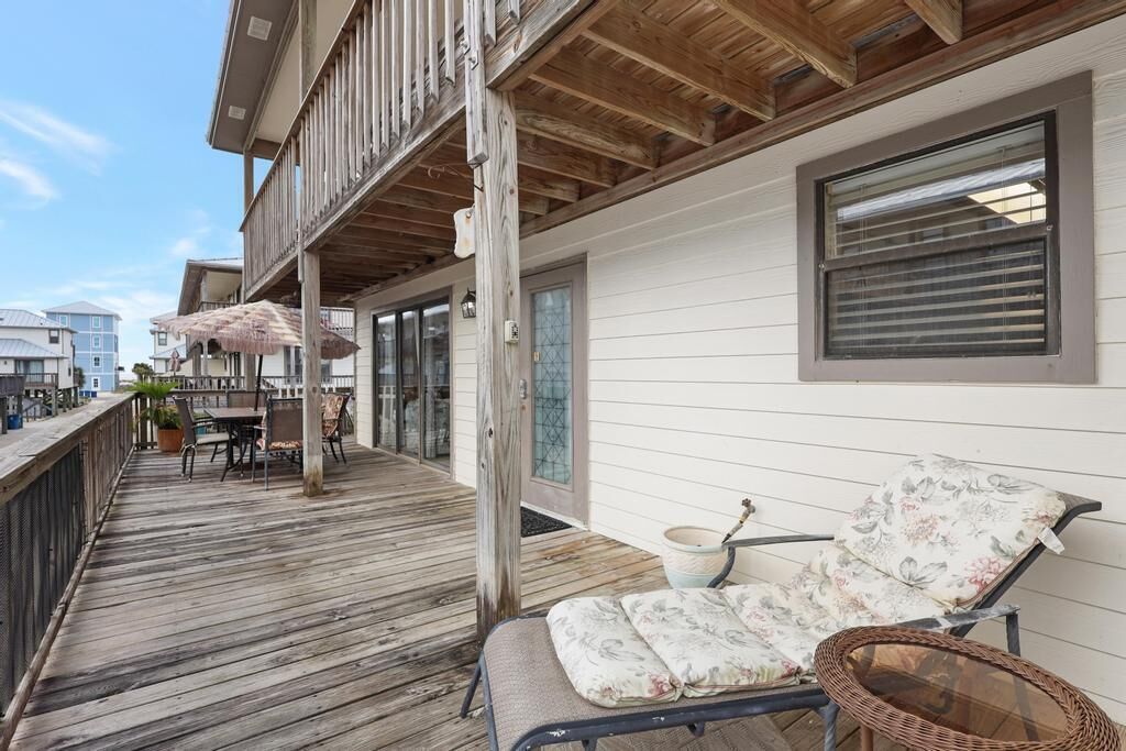 A wooden deck with a lounge chair and a table, overlooking a body of water.