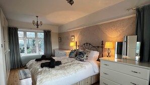 A bedroom with a large bed, a dresser, a nightstand, a lamp, a mirror, and a window with curtains. - Spacious, Stylish House - 500 yards to the sea front (West Cross)