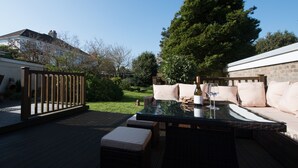 An outdoor patio with a glass-top table, cushioned seating, and a wine glass. - Spacious, Stylish House - 500 yards to the sea front (West Cross)