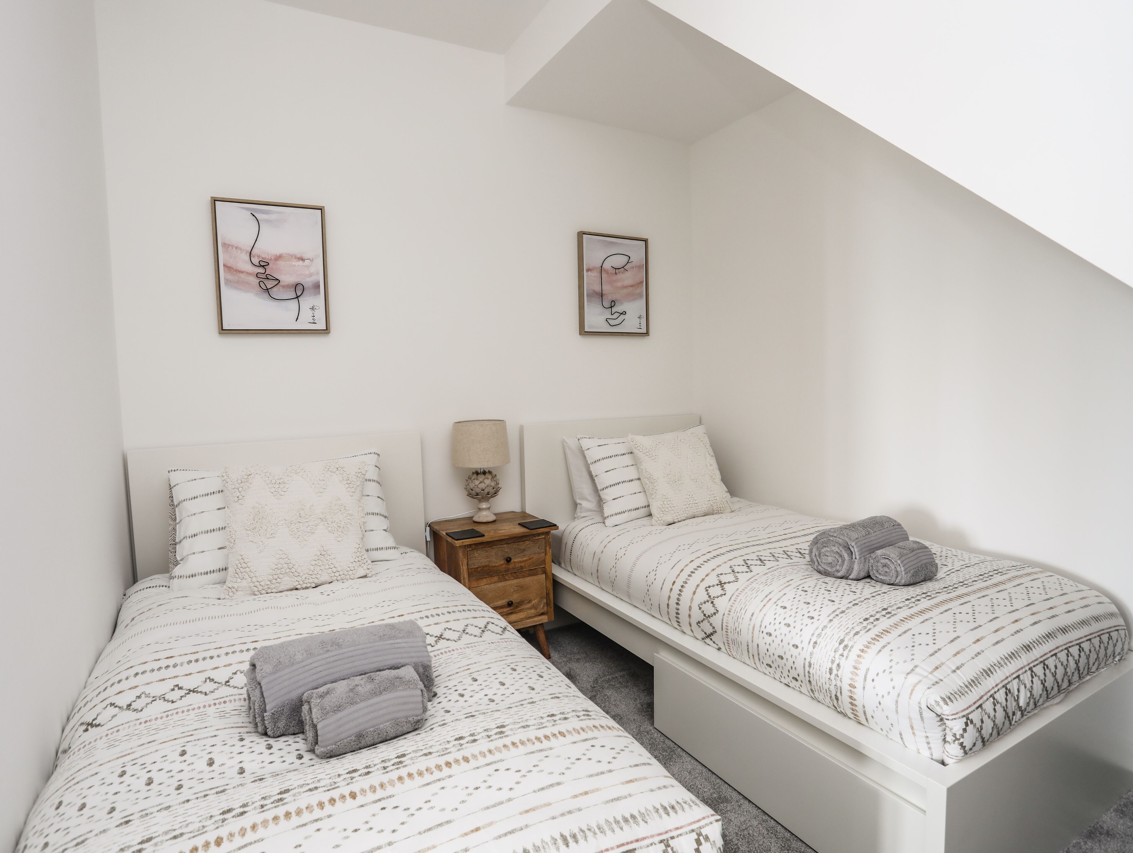 A bedroom with two beds, a nightstand, and two framed pictures on the wall.