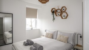 Une chambre moderne avec un grand lit, un miroir, une fenêtre et un luminaire en bois au plafond.