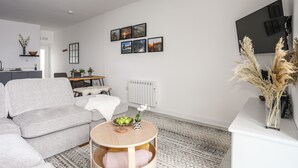 Un salon moderne avec un canapé gris, une table basse ronde et un coin repas comprenant une table et des chaises en bois.