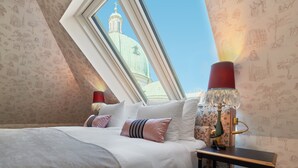 A bedroom with a skylight, a bed with white bedding, a red lamp, and a wall with patterned wallpaper. - The Leo Grand (Vienna)