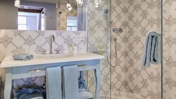 A bathroom with a white sink, two towels, a glass shower enclosure, and patterned wall tiles.